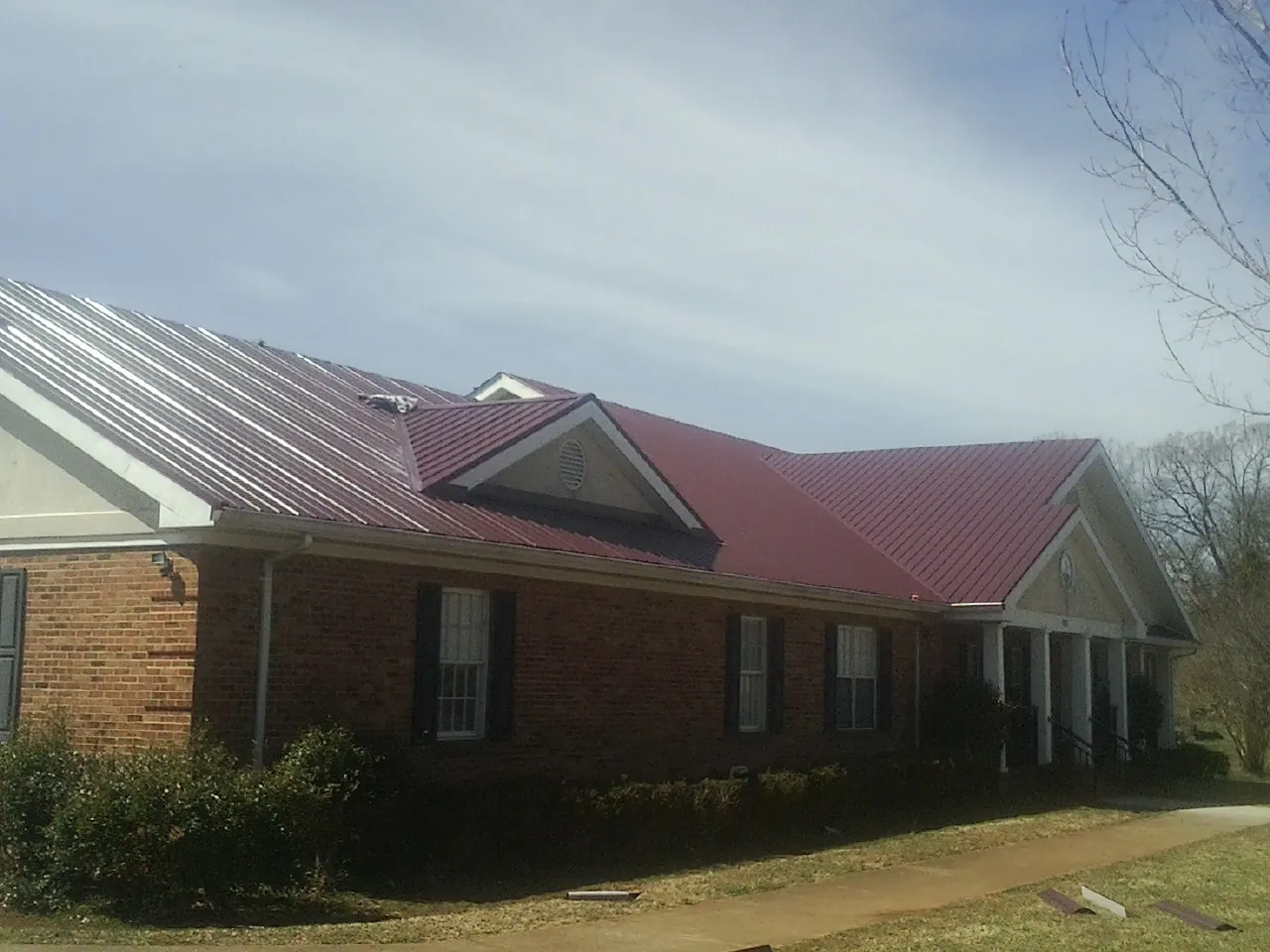 Red metal roof with gabled entries on a long brick building, from a Hail Damage Roof Repair job in Sherrard