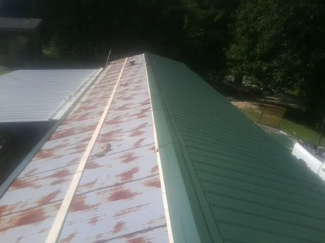 Old rusted panels beside newly installed green metal roofing — Wind Damage Roof Repair by Roofing Brothers in Sherrard