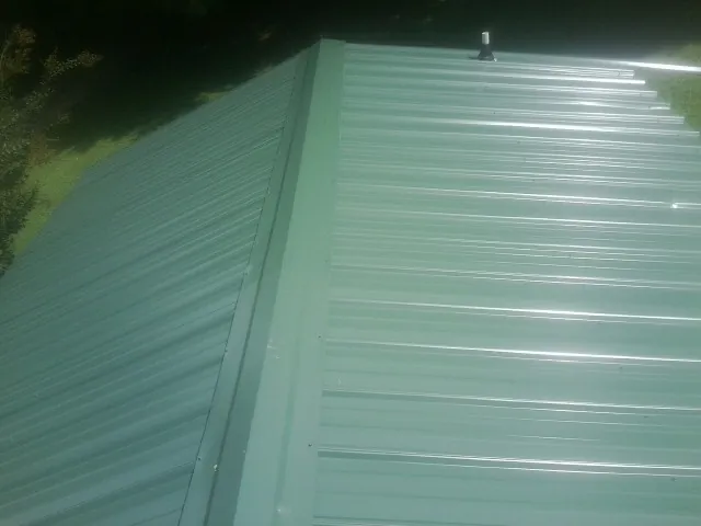 New green metal panels meeting at the ridge of a roof — Flat Roof Repair work by our crew in Sherrard