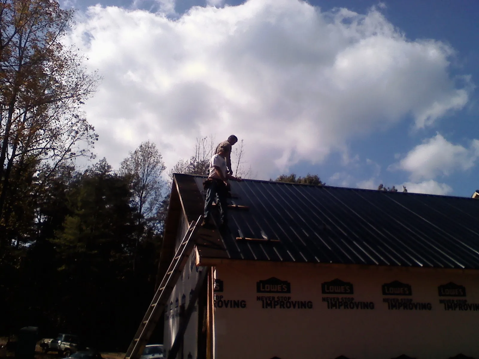 Roofer fastening dark metal panels high against a cloudy sky, from a Roof Inspection job in Sherrard