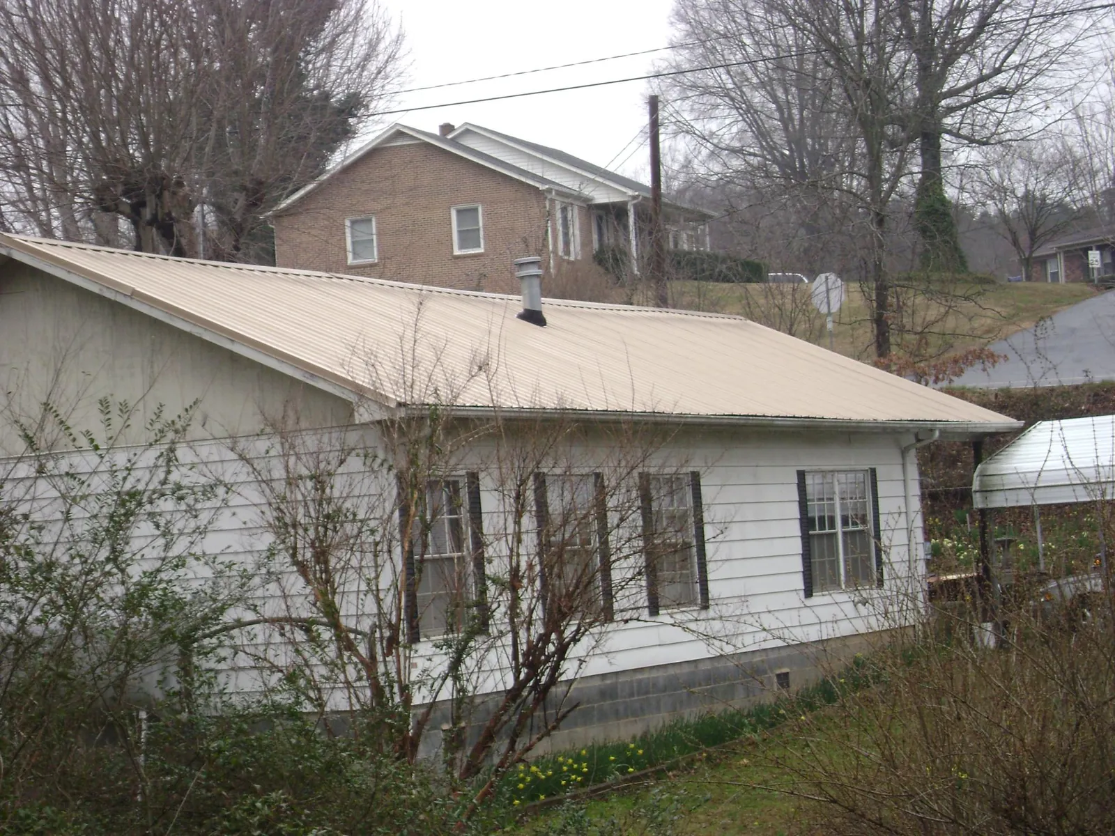Tan metal roof on a white sided house set into a hillside — Commercial Roofing by Roofing Brothers in Sherrard