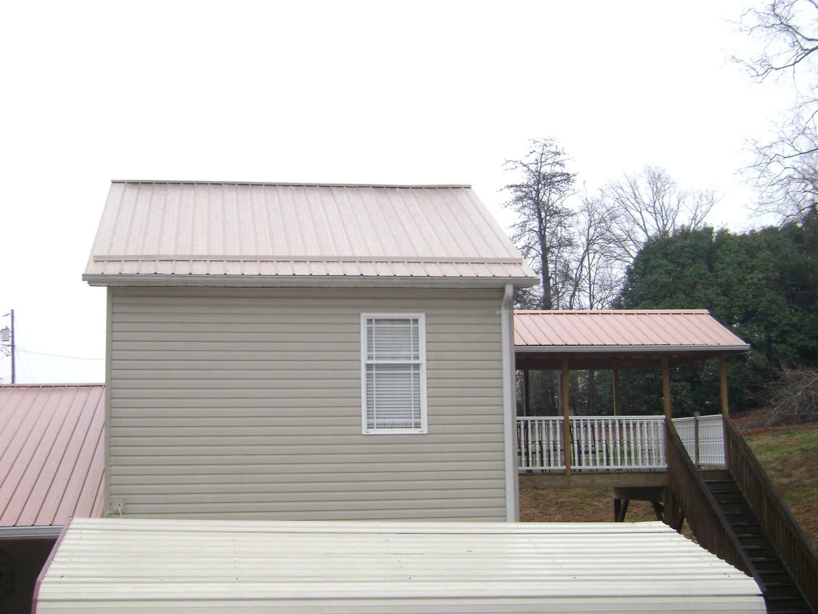 Tan metal roofs on a two story addition and attached porch, from a Roof Replacement job in Sherrard